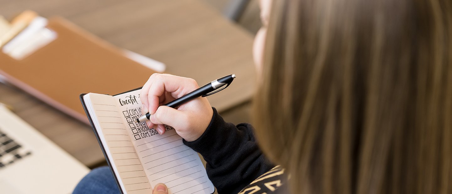 Transfer Information An Oakland University student making check marks next to courses listed in a notebook.