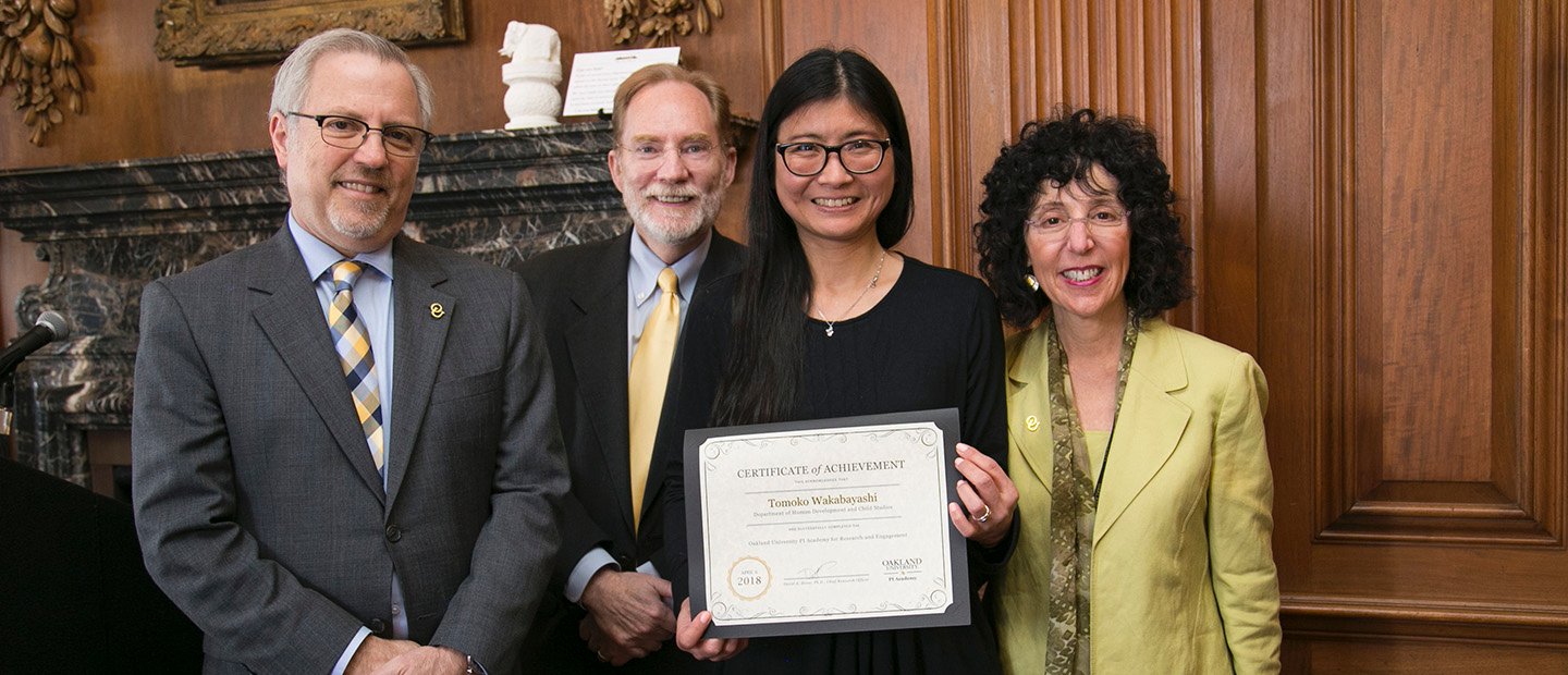 The Oakland University PI Academy for Research and Engagement Four people posing for a group photo. One woman is holding a certificate.