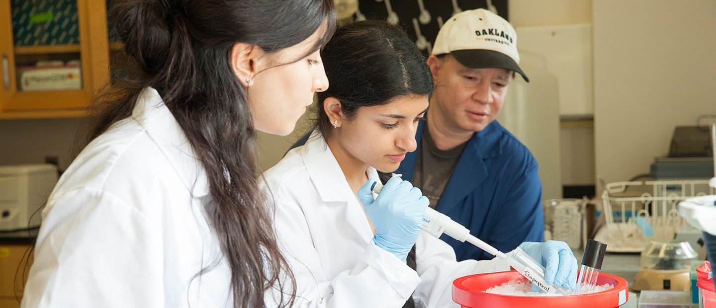 Student Funding Opportunities A woman holding a vial in a lab while two people observe.