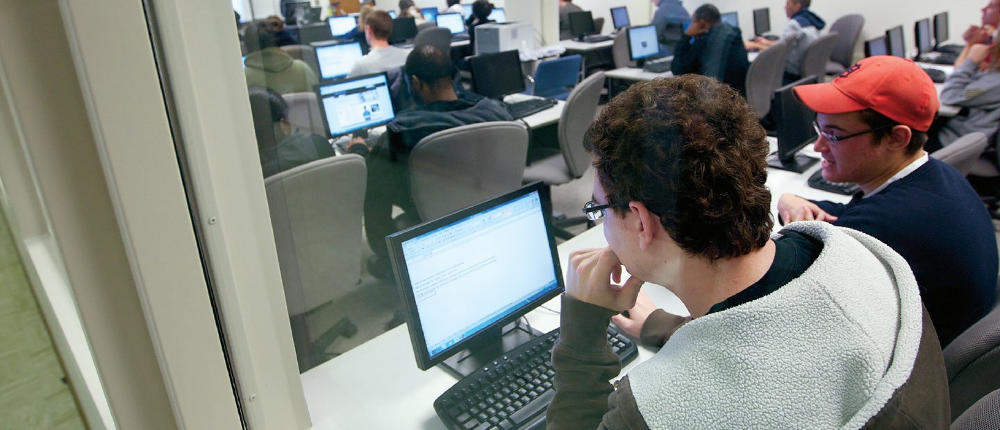 Computer Science view from behind of students seated at long white tables with computers