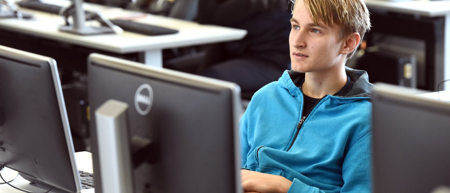 Information Technology student in a blue shirt seated at a computer in a classroom