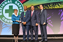 image of four men and one woman in professional attire standing on a stage with a sign in the background reading "National Safety Council"