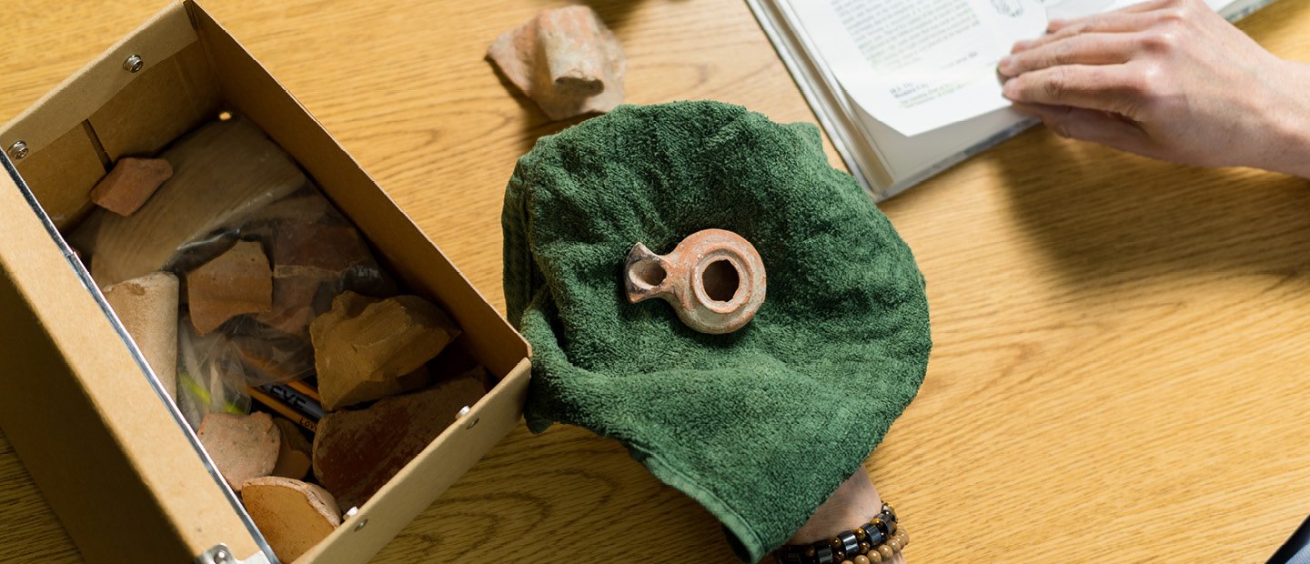 Support Our Programs An artifact resting on a green cloth, next to a box of similar items.
