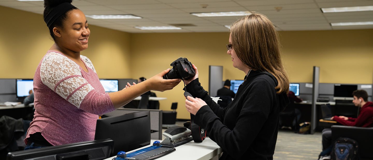 young woman showing another young woman how to use a digital camera