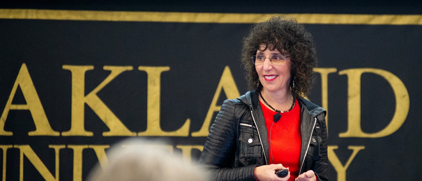 President Ora Hirsch Pescovitz standing in front of a black and gold Oakland University banner.