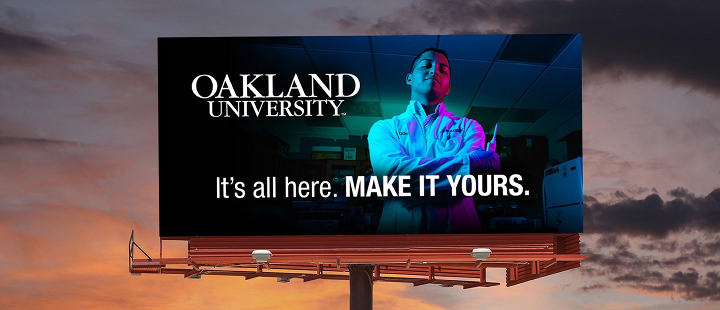 A billboard featuring a young man and the words "Oakland University. It's all here. Make it Yours."