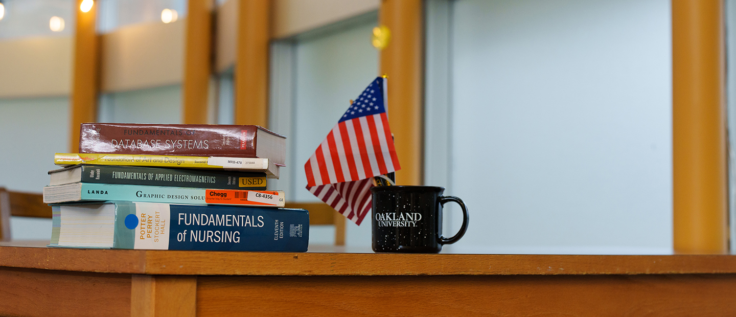 Books stacked on a desk next to an American flag and coffee mug