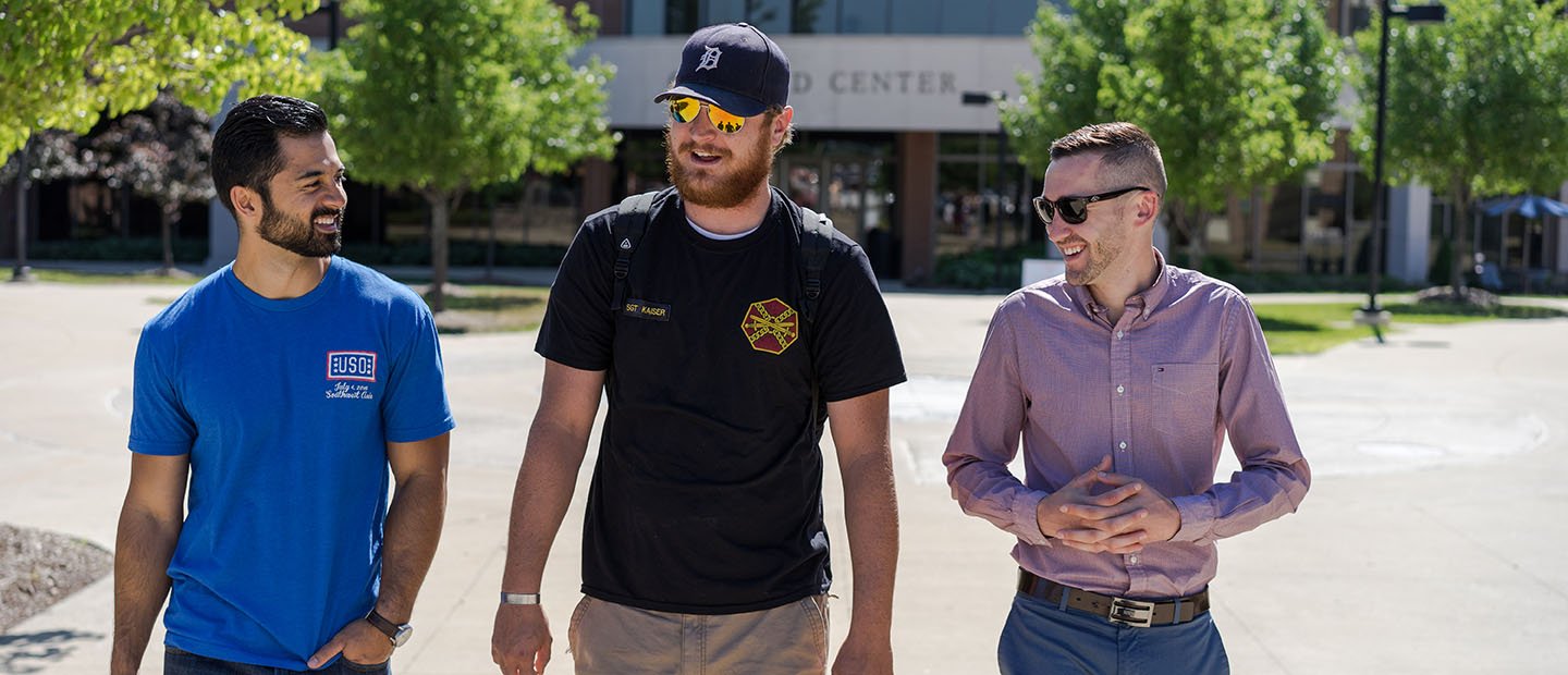 three men walking and talking outside of the Oakland Center building