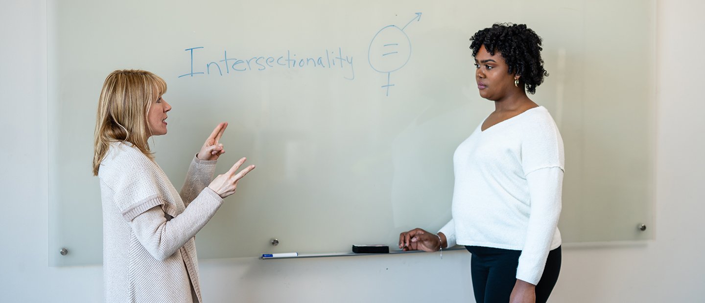 Two women standing in front of a white board