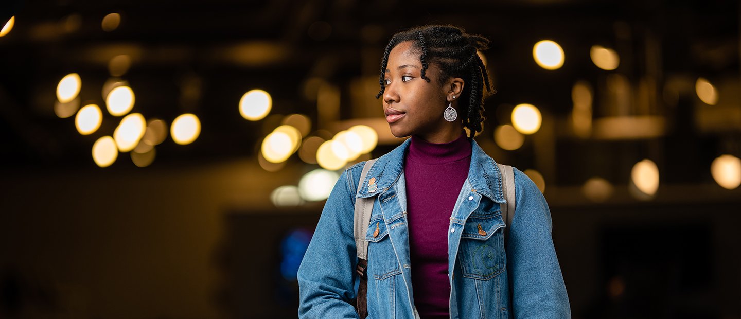 young woman looking off to the side, blurred lights behind her