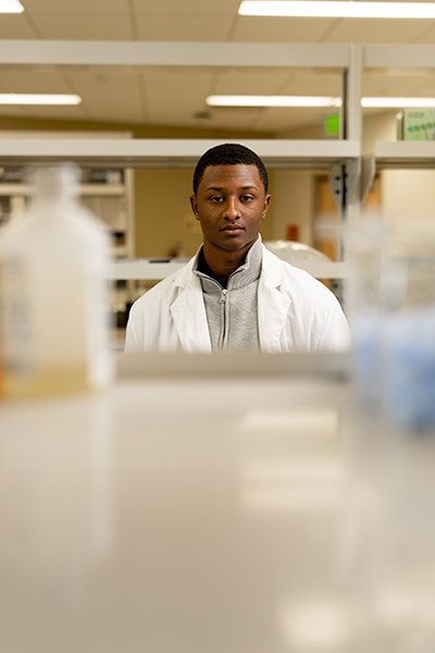 Student in a lab coat standing in a lab.