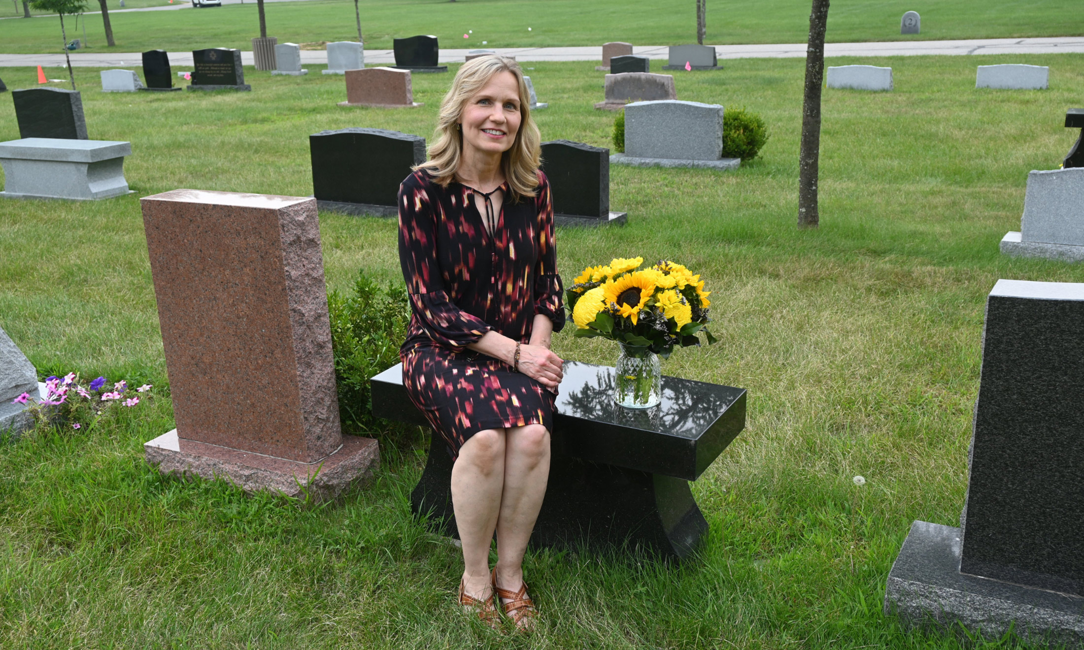Woman seated at cemetery grave with flowers