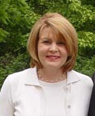 woman in a white shirt and sweater standing outside, smiling at the camera