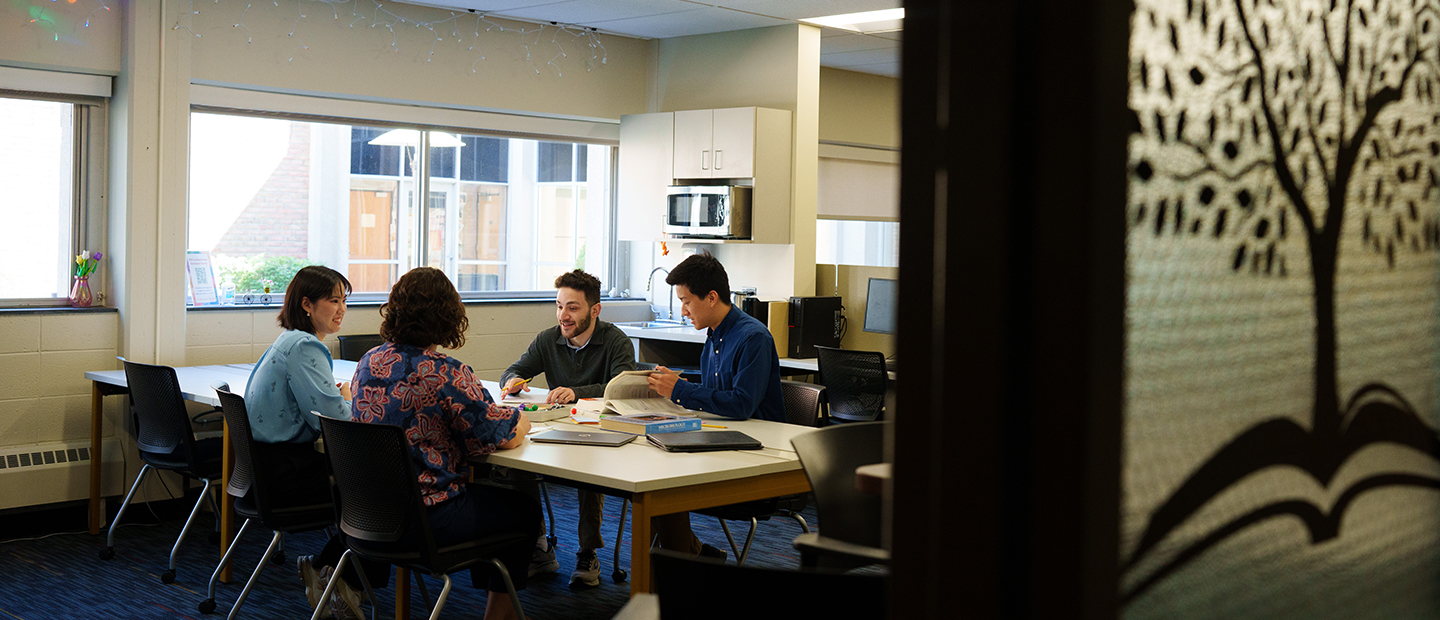 Four people sit around a desk talking and studying in the Bio Learning Lounge.