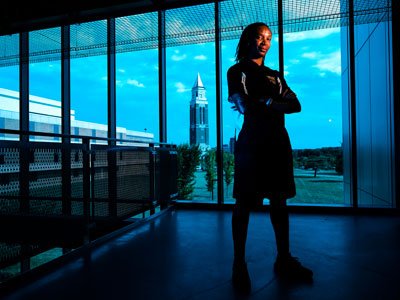 Woman with arms crossed standing in front of a row of windows in a building
