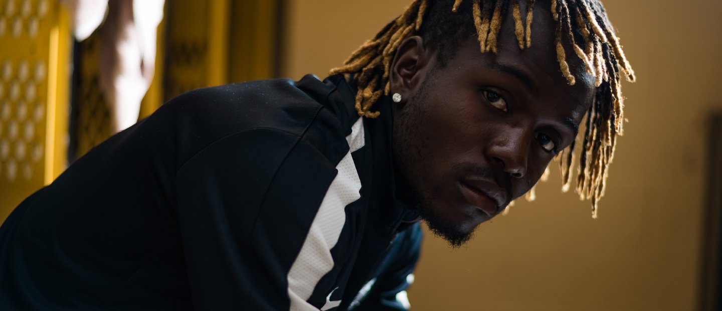 Male athlete hunched over sitting on a bench in a sports locker room.