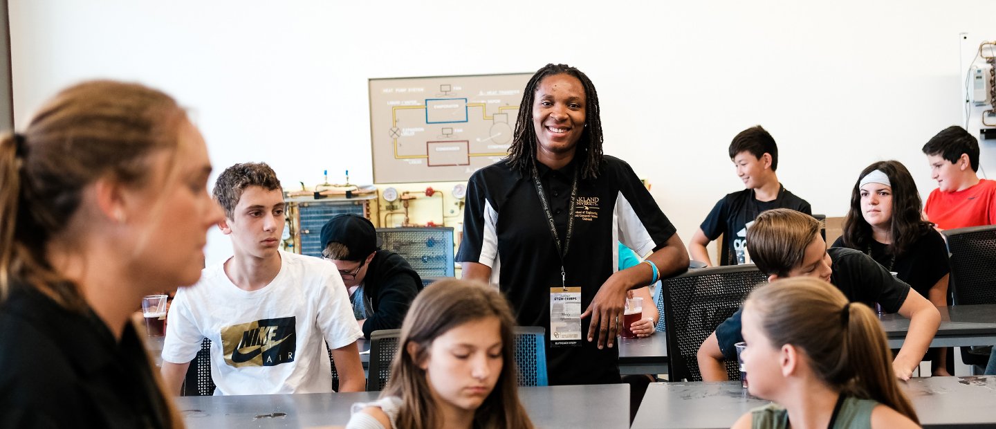 Female Teacher standing in the middle of a classroom full of students
