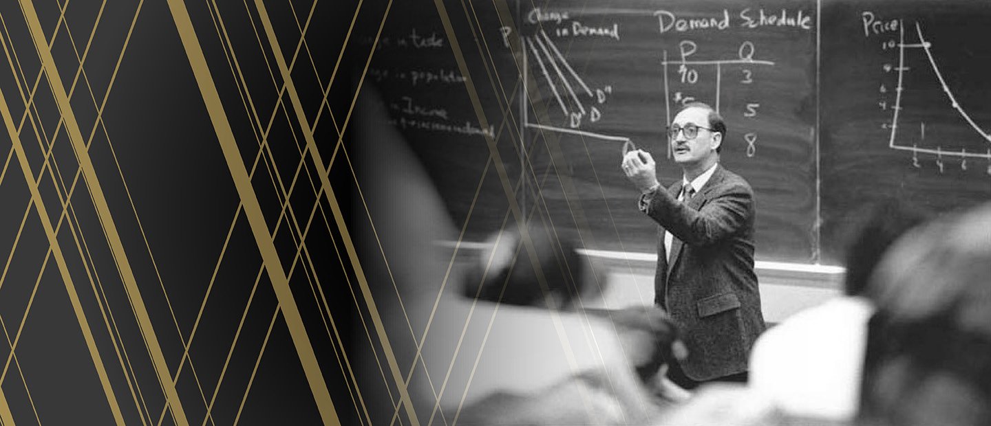 A black and white image of a professor in front of a chalkboard, facing the class.