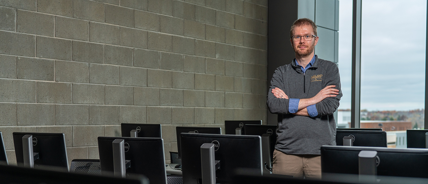 A man with his arms folded posing for a photo in a computer lab