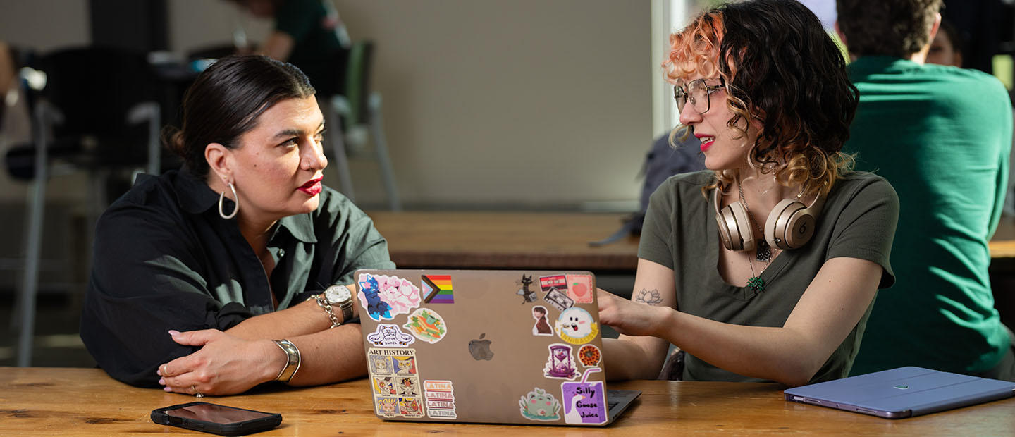 Two students talking over an open laptop