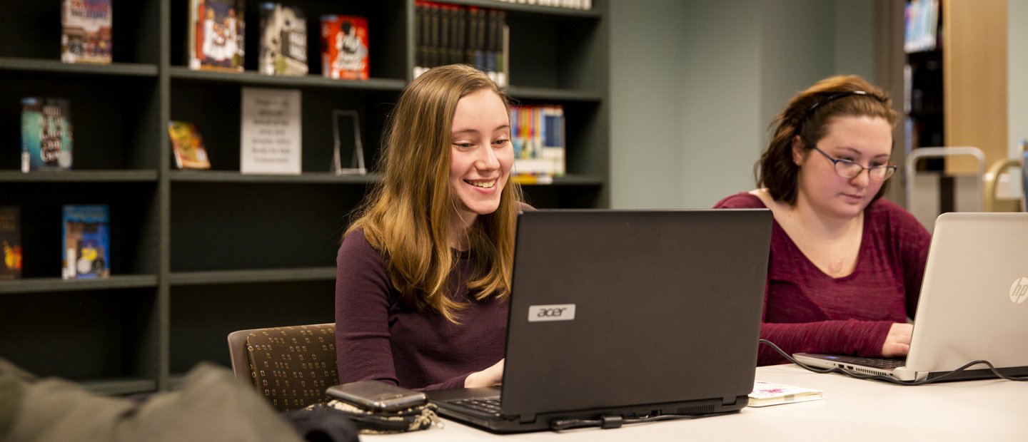 A woman smiles as she looks at her laptop computer screen.