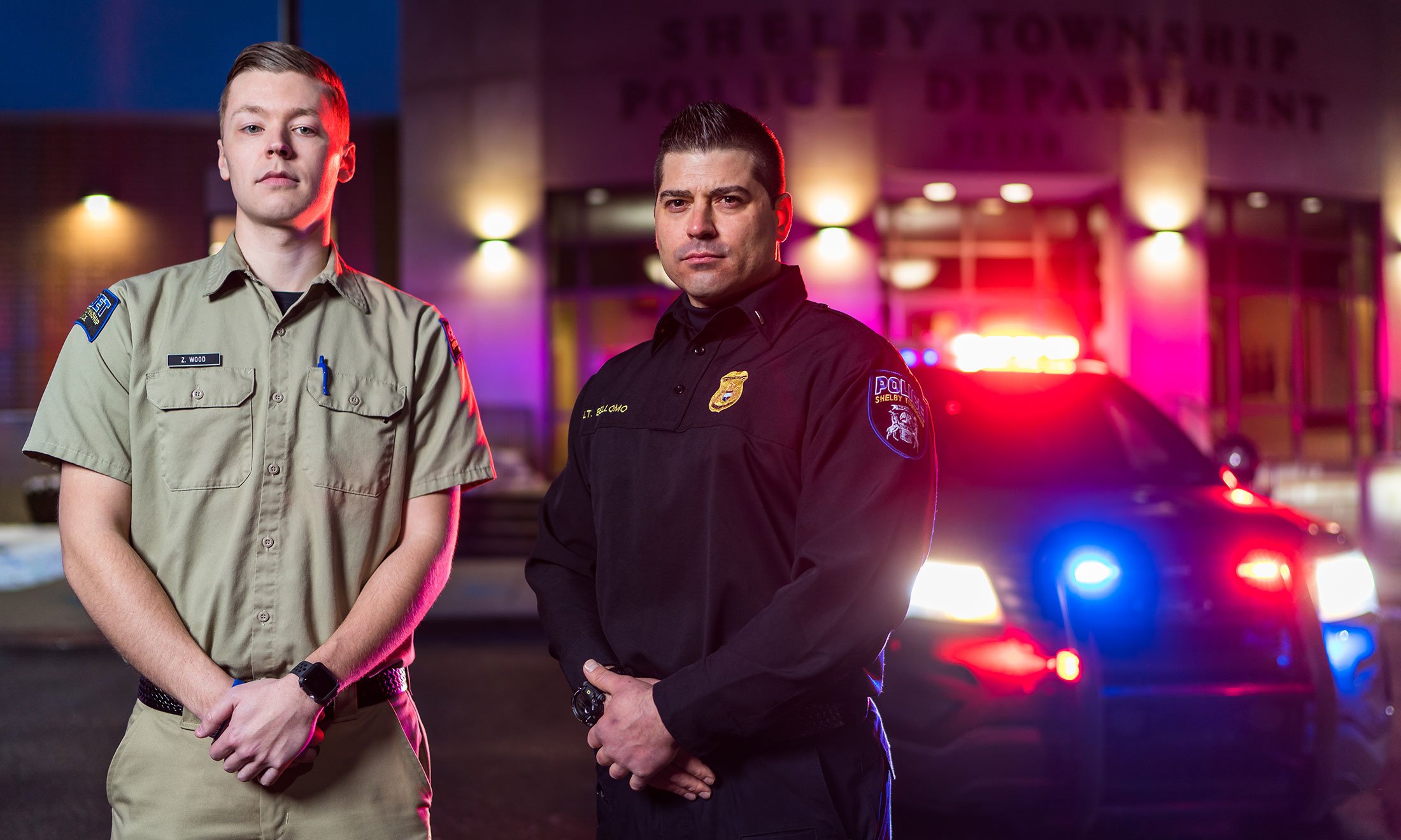 Two men posing in front of a police car.