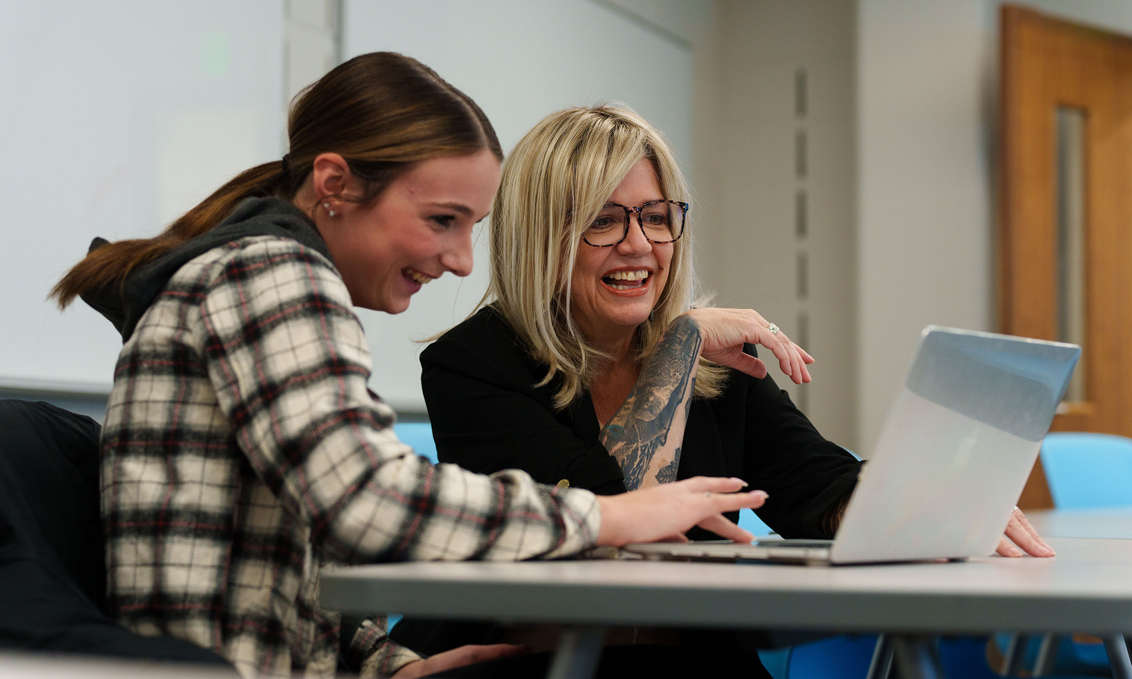 A professor and student look at a lap top and smile.