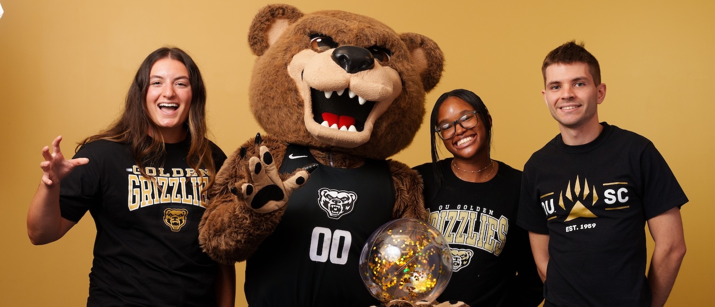 Three Oakland University students posing with the Grizz bear mascot