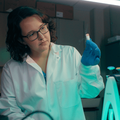 A woman in lab coat looks at a test tube.