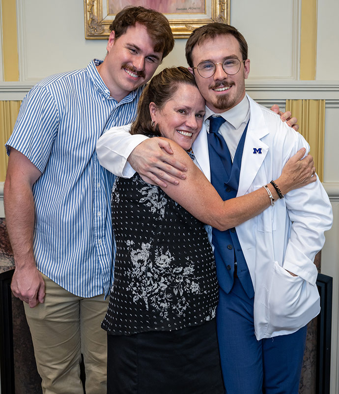 Kyle, wearing a white coat, hugs mother and brother