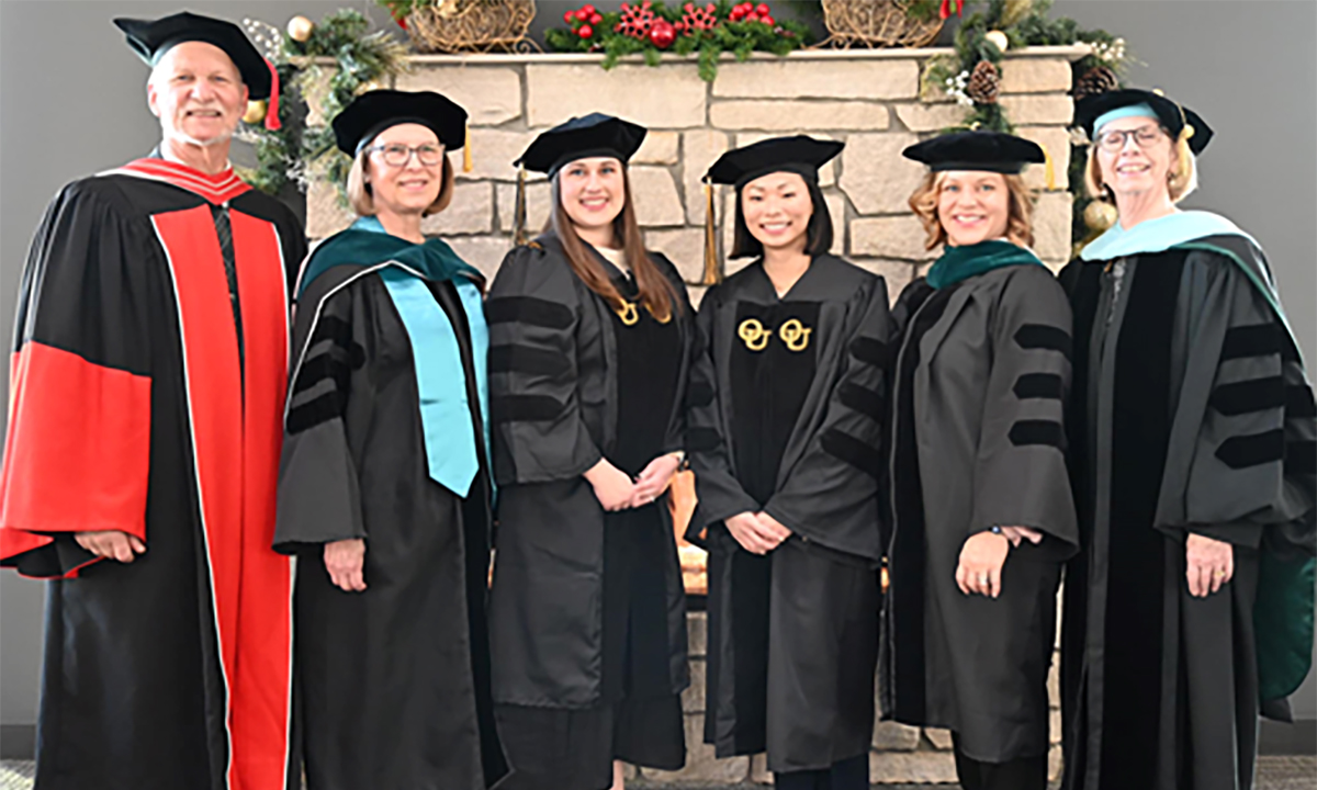 Group of people standing smiling at camera with graduation gowns on.