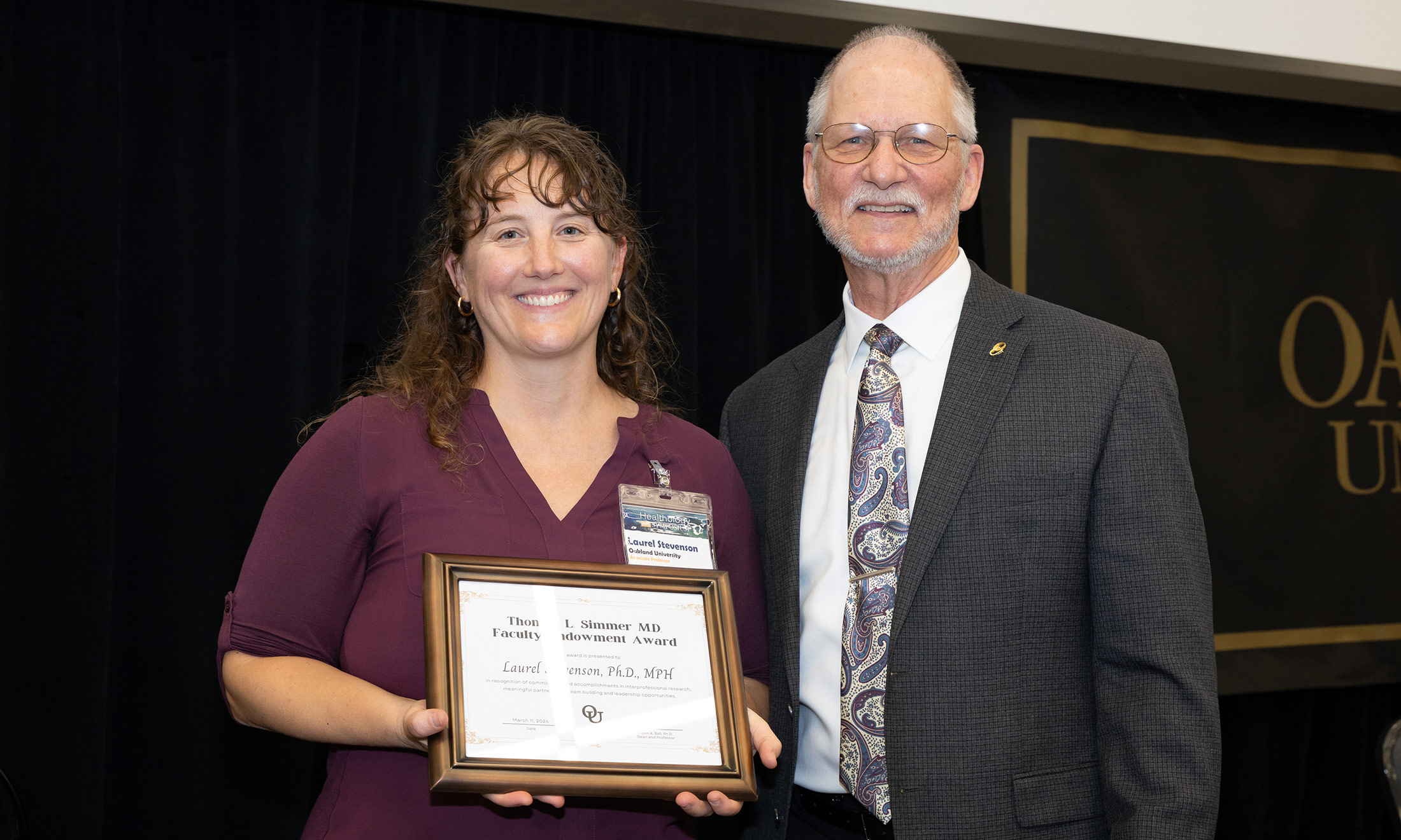 Dr. Laurel Stevenson holds an award, with Dr. Kevin Ball