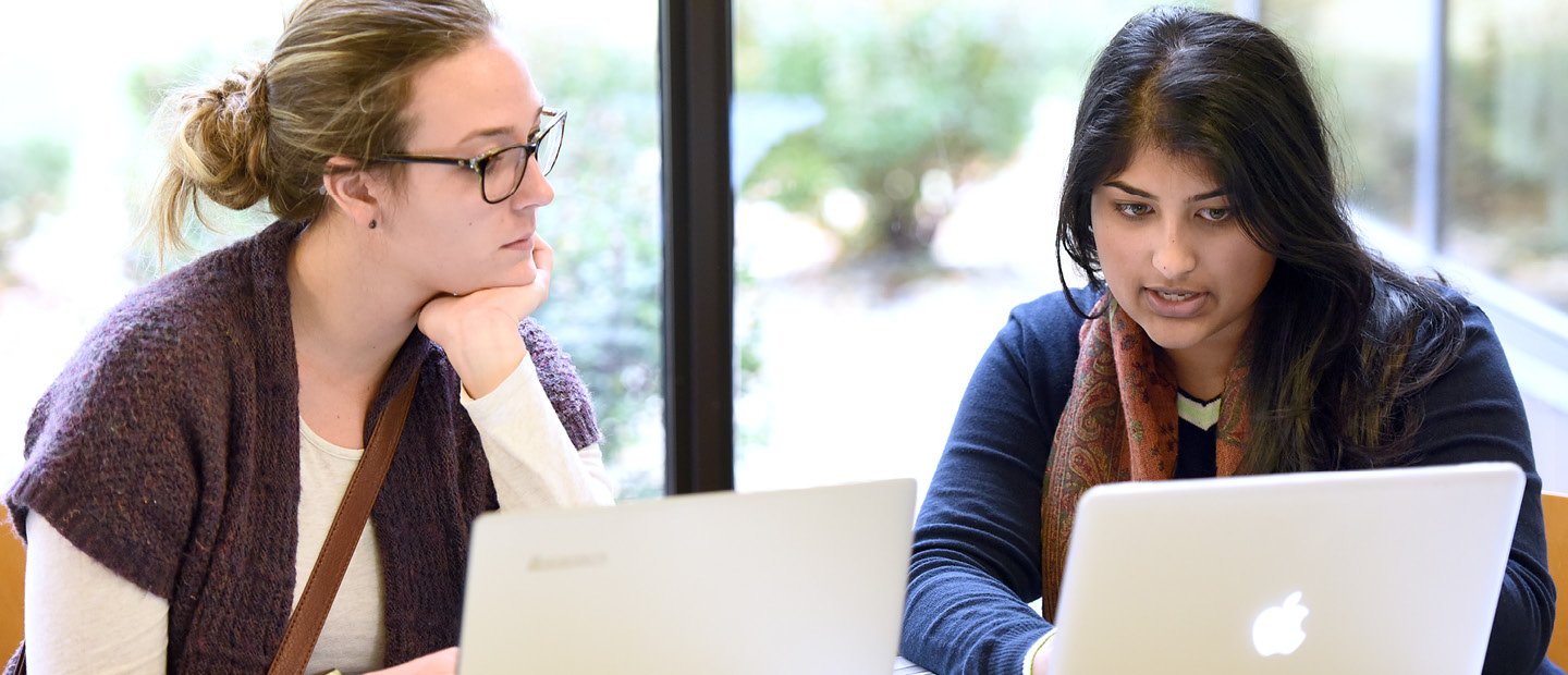 two women seated behind open laptops