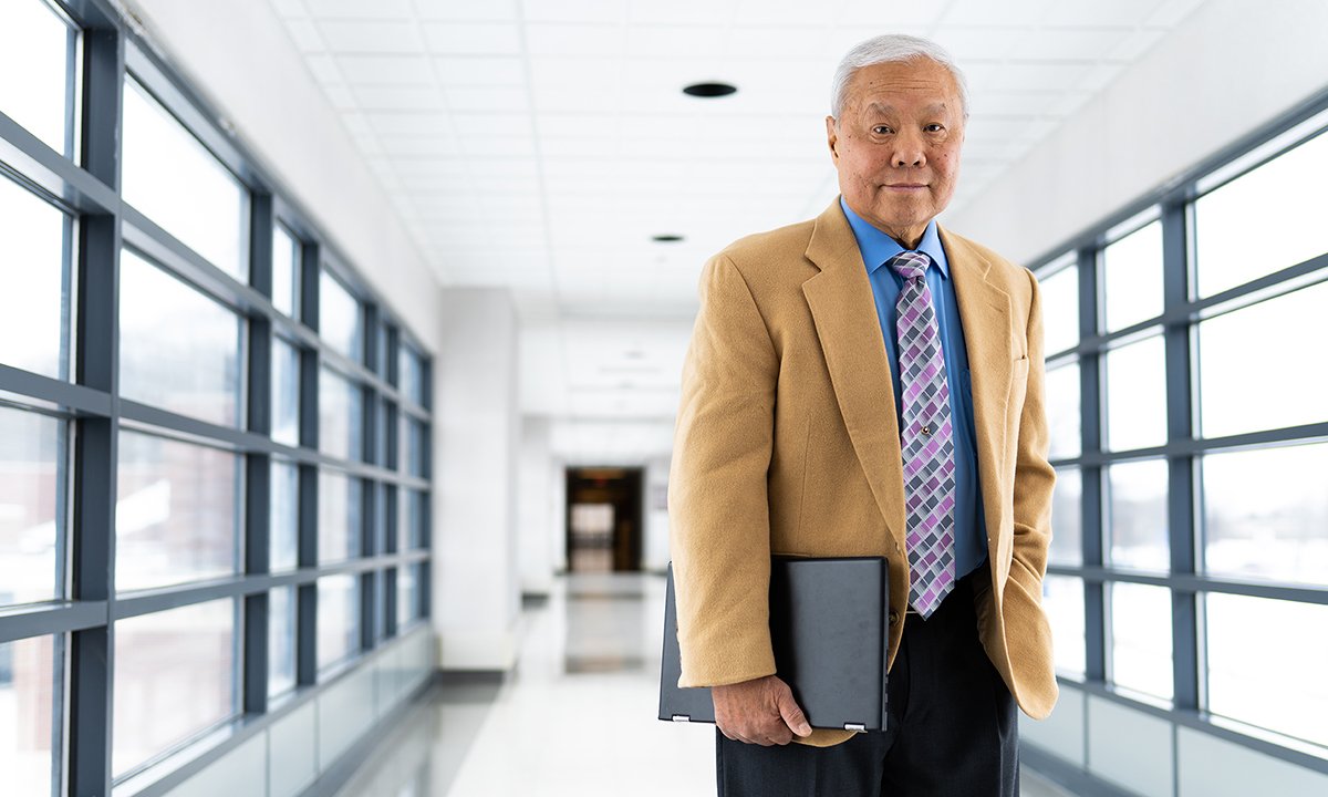 A man standing in a hallway, holding a folder.