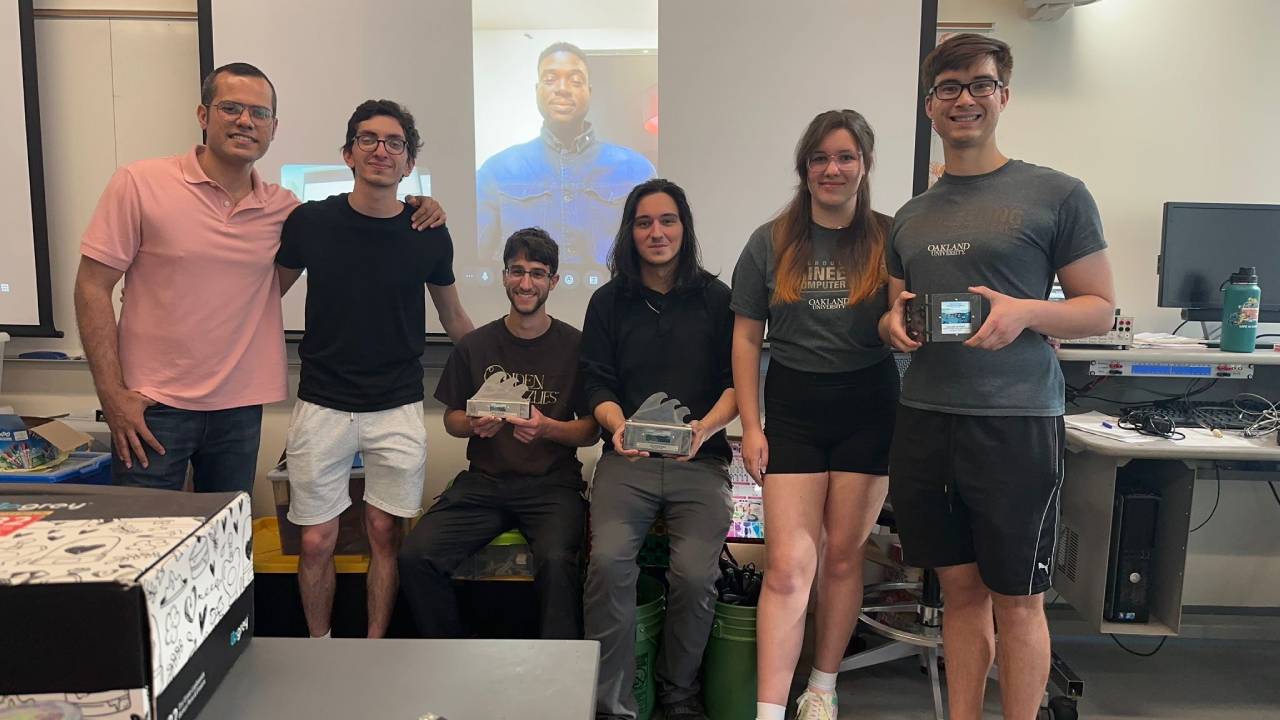 Marine Energy team members standing in a lab with one shown virtually on a projector screen