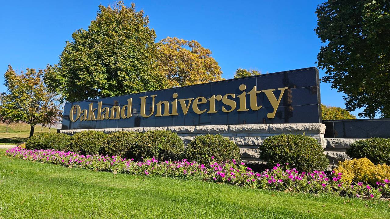 Oakland University signage in summer with blue sky and flowers