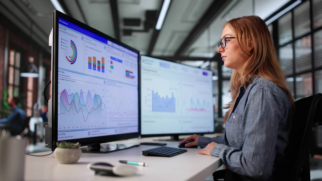 Business student sitting at desk looking at computer monitors