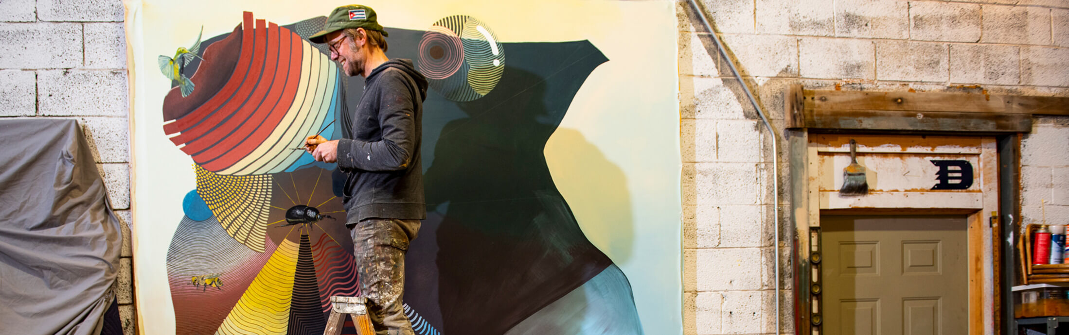 A man on a ladder painting a mural