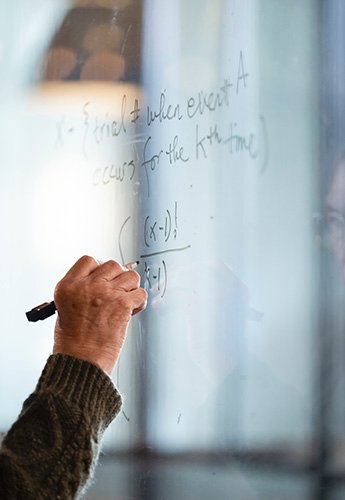 A hand writing on glass with a dry erase marker