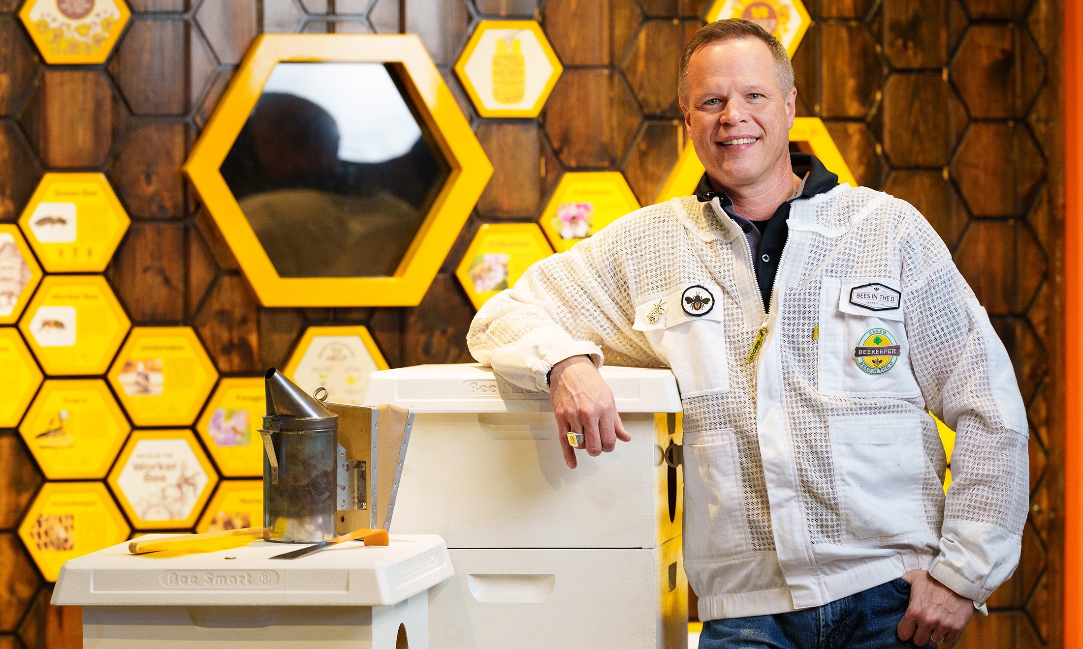 A person leaning on a bee box with decorative honeycombs behind him