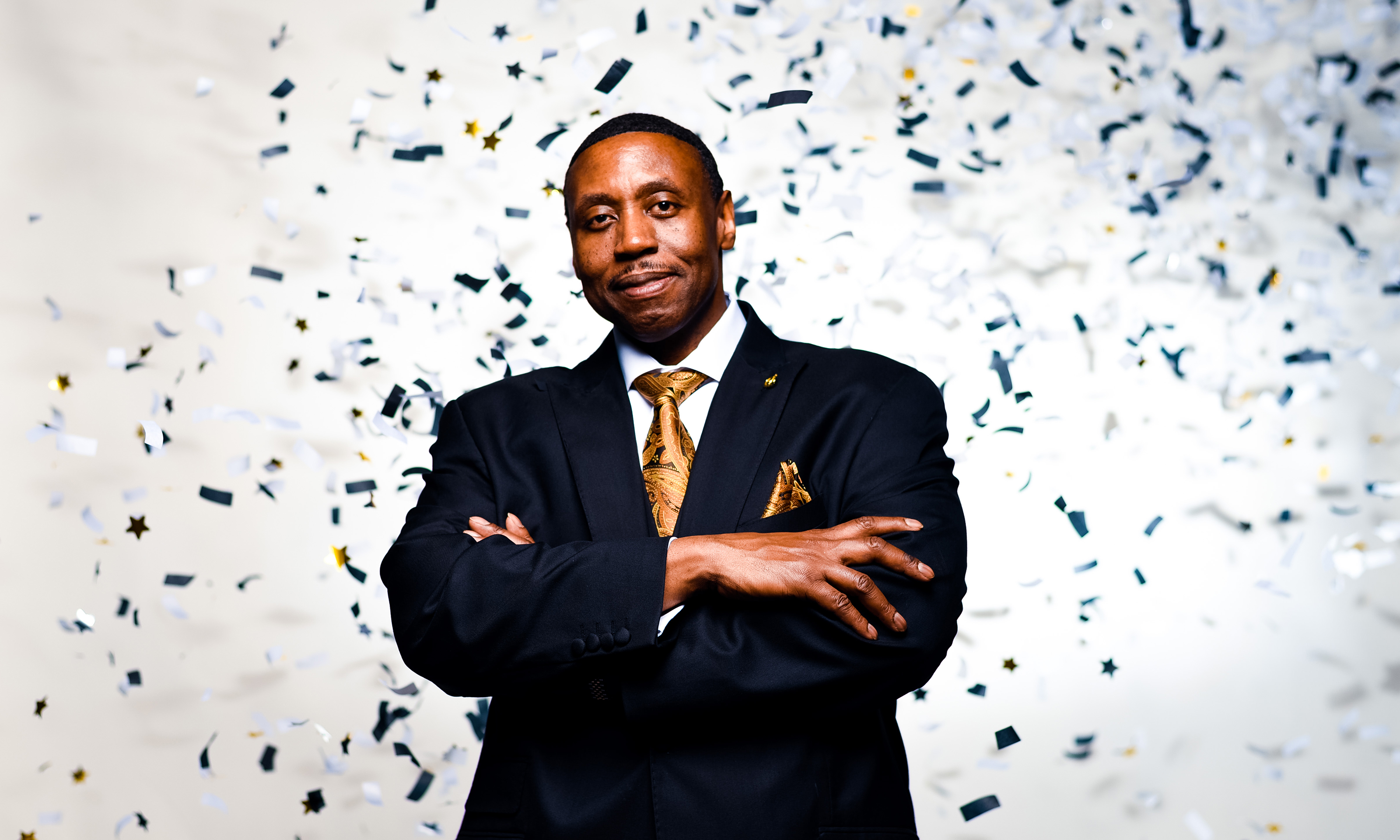 A man standing with his arms crossed in front of confetti