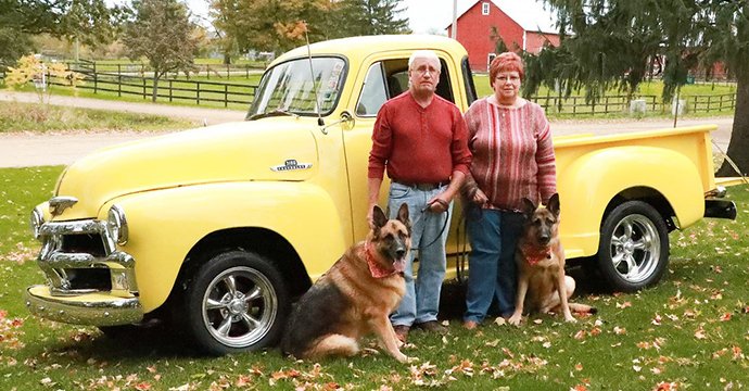 Two people and a dog in front of a pickup truck