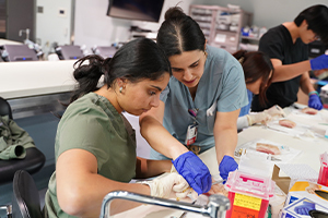 A resident shows a medical student how to suture