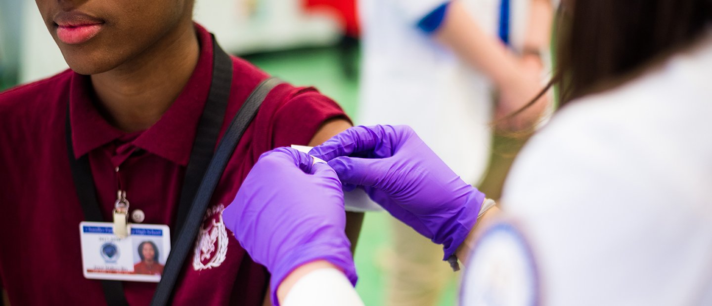 Person wearing purple medical gloves, applying a bandage to a person's arm.