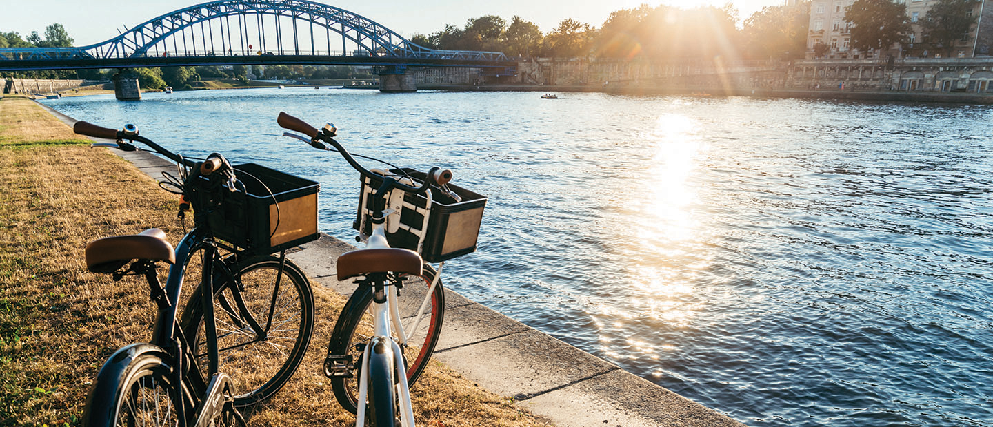 Two bikes parked on grass next to river with bridge in background