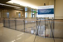 A sign that says Healthology Symposium on a stand in an empty hallway.