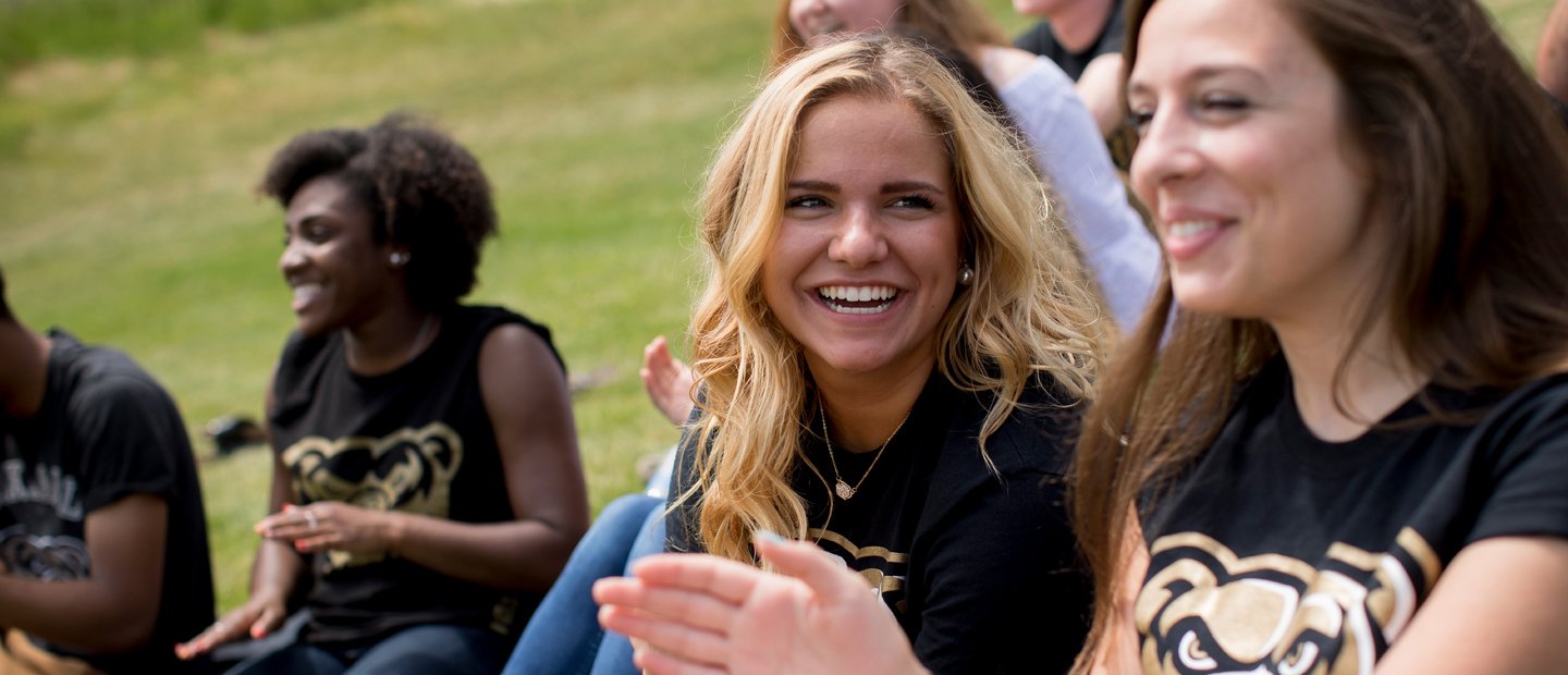 Female student, sitting outside, laughs with a group of friends