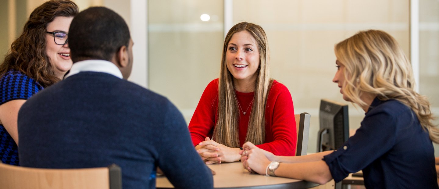 _0002_Master of Arts in Counseling.jpg Four people seated around a table, smiling and talking.