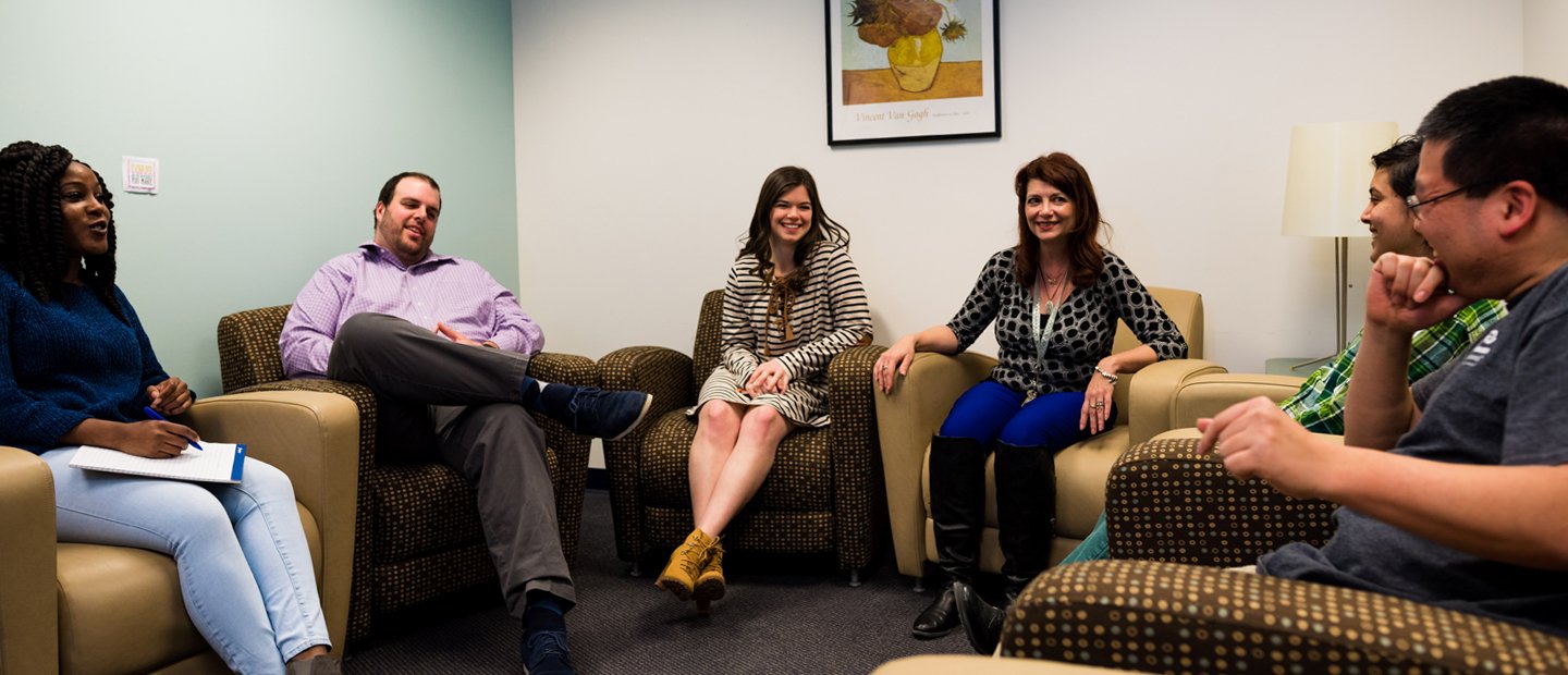 Six people seated in arm chairs, facing each other, smiling and talking.