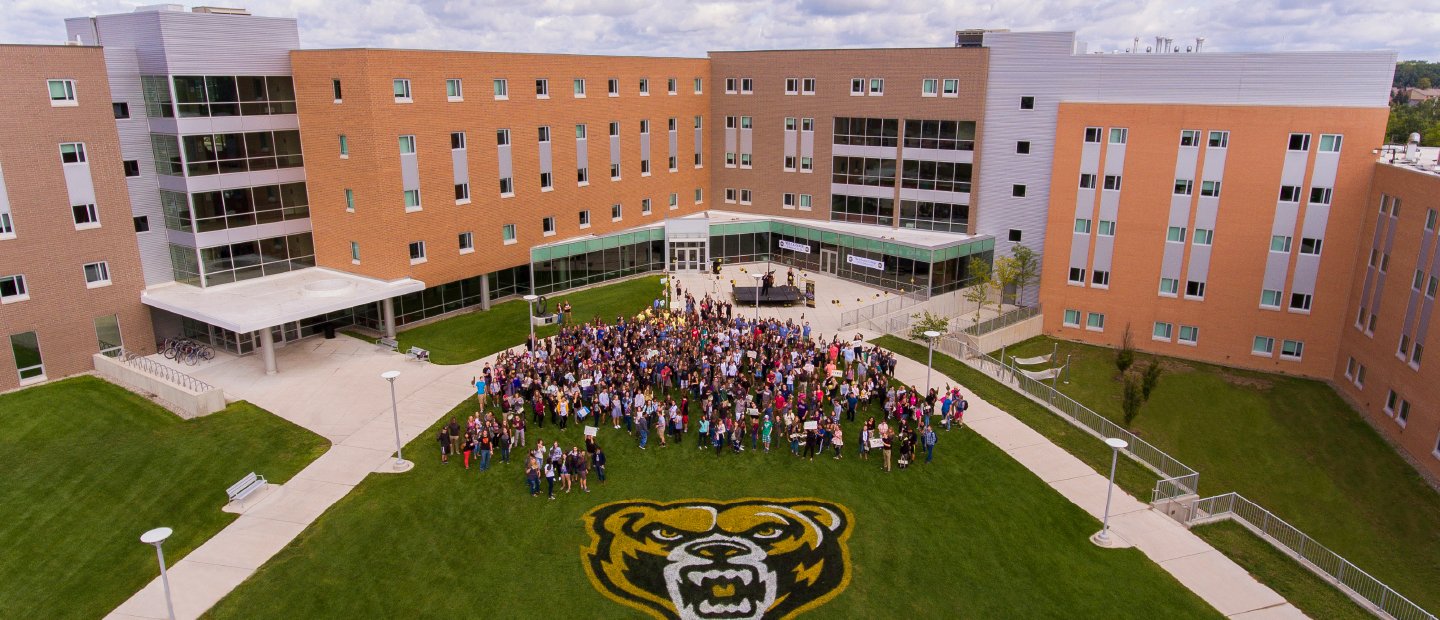 Aerial shot of large group of HC students stand on O U campus with large Grizz mascot painted on the ground